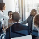 A diverse team of professionals in a collaborative meeting where a saleswoman stands presenting, an example of a sales strategy for alignment and buy-in.